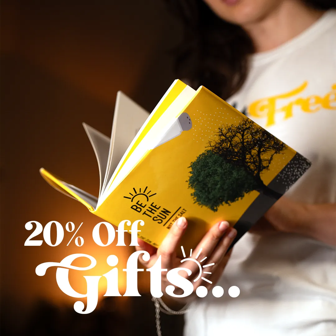 Person holding an open yellow book with a tree and sun illustration on the cover and text 'Be The Sun', with a 20% off gifts promotional text overlay.