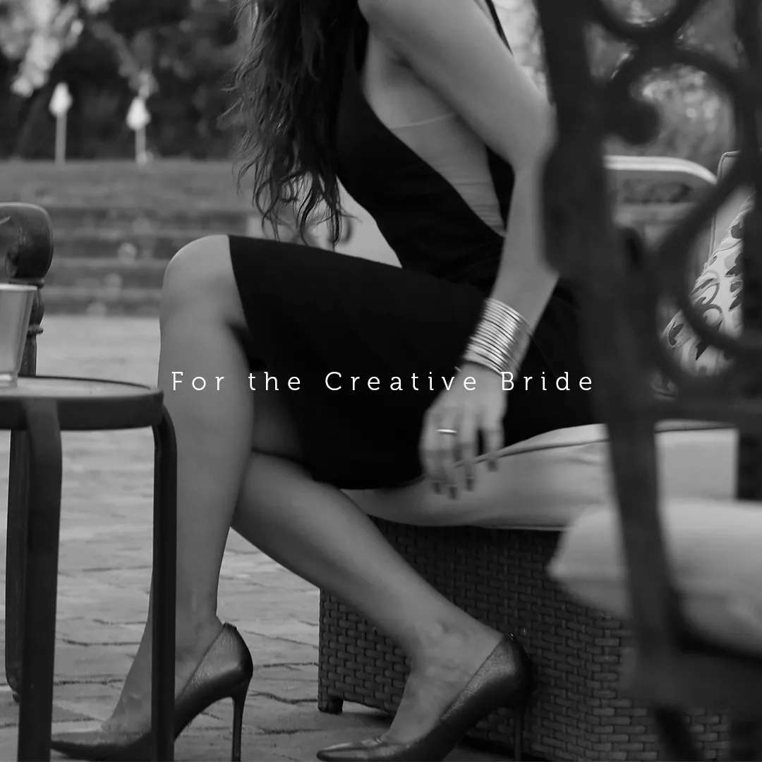 Black and white photo of a woman sitting on a wicker chair outdoors, wearing a black dress and high heels, with the text 'For the Creative Bride' overlayed.