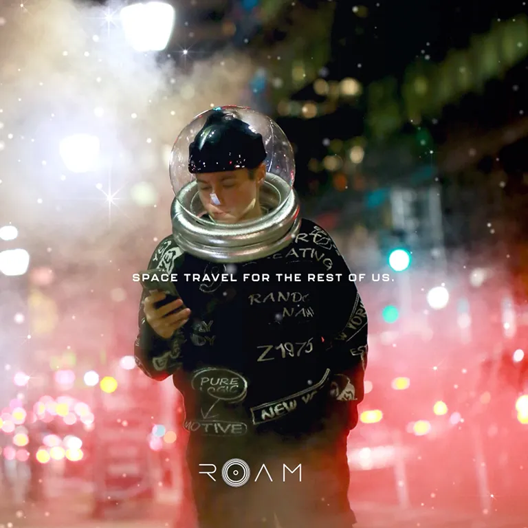 Person wearing a modern spacesuit helmet and a black jacket looking at their phone, with city lights and misty atmosphere in the background, text reads 'Space Travel for the Rest of Us' and 'ROAM'.