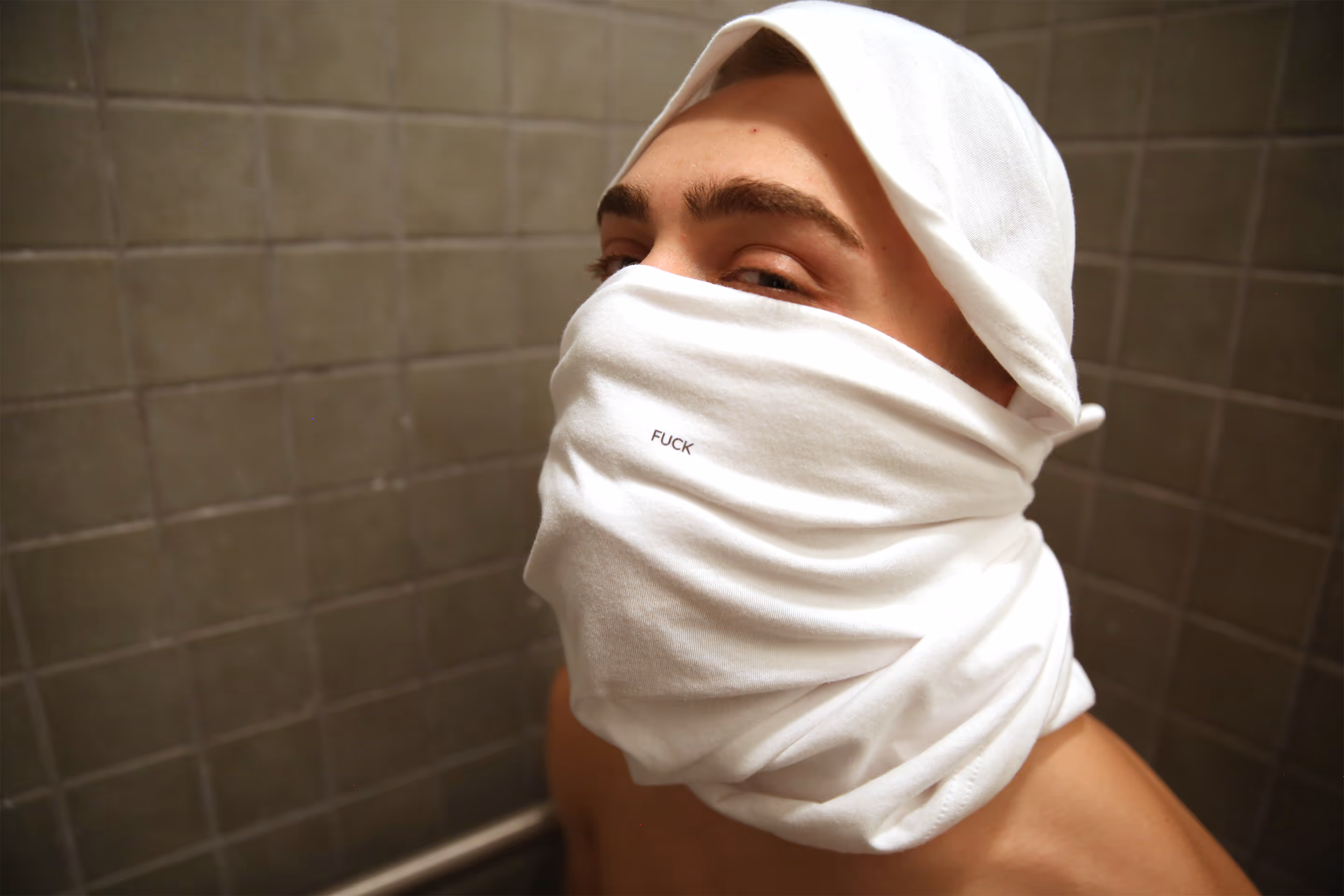 A black and white picture of a person holding a TKINK designer white t-shirt with a small printed "FUCK" over their head.